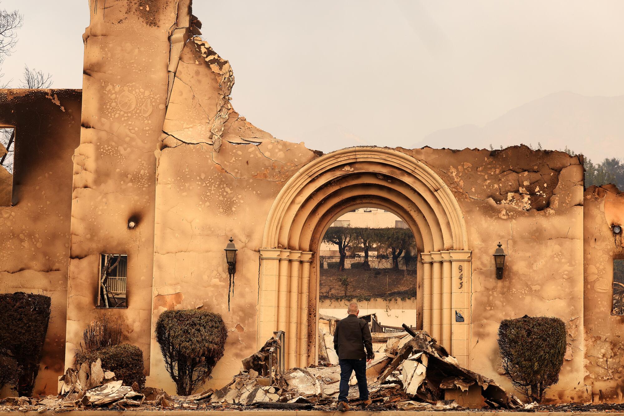 A person stands near the arched entryway of a gutted building.