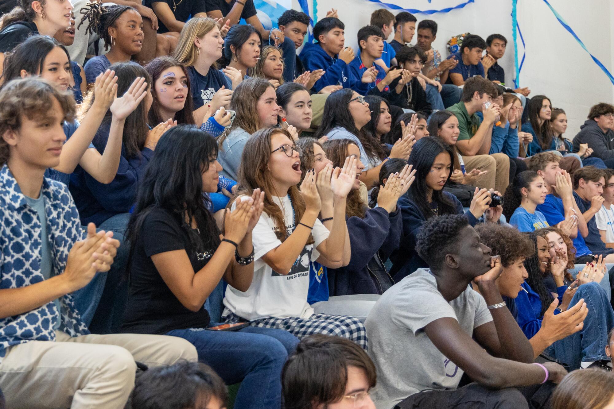 Macayla Story (center, white T-shirt) sits on bleachers surrounded by classmates and claps