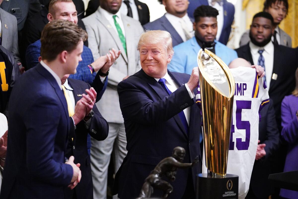Tigers Quarterback Joe Burrow gives President Trump a team jersey while the team looks on.