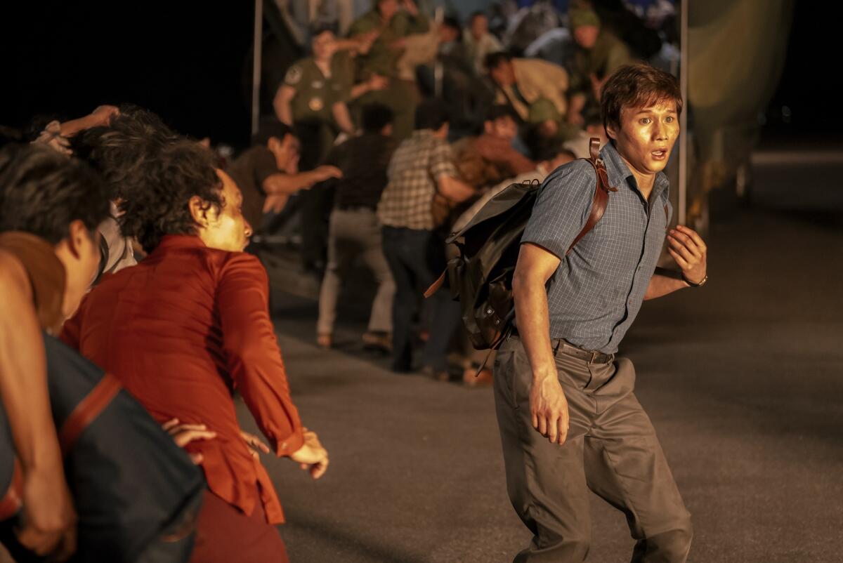 A man wearing a backpack looks out as people run toward the open hatch of a plane.