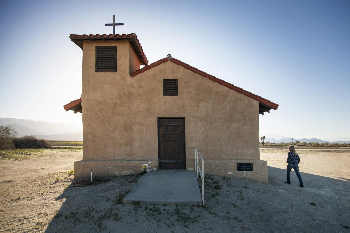 Douglas McCulloh photo. A woman walking around a small stucco chapel with bell tower.