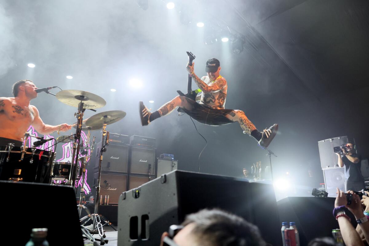 Drummer Isaac Holman plays while Laurie Vincent leaps in the air with his guitar