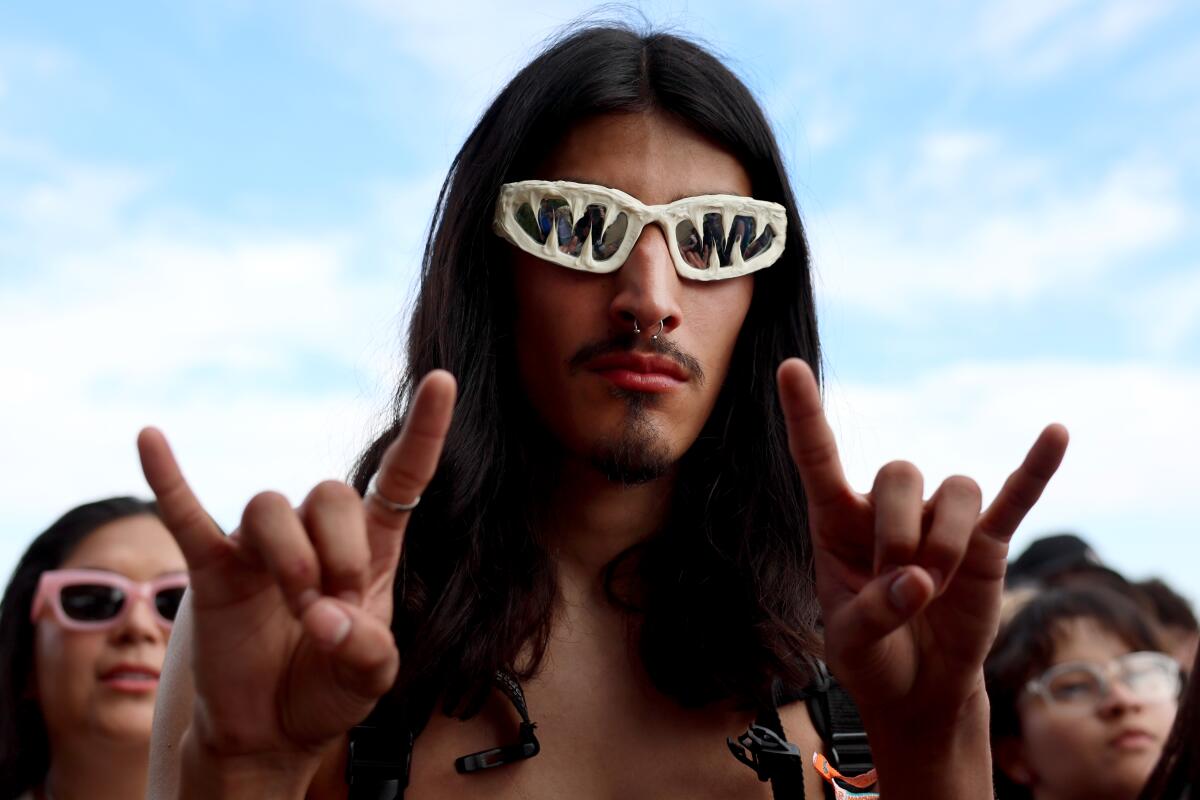 A miusic fan raises the rock horns and has shark tooth style sunglasses
