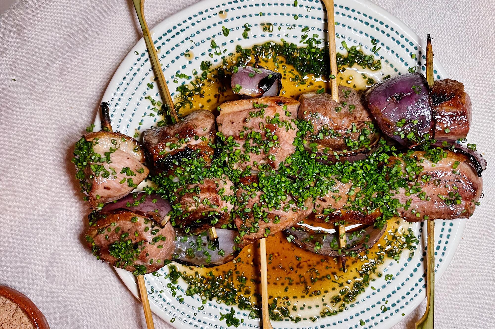 An overhead photo of five duck breast skewers with black-garlic jus and chives.