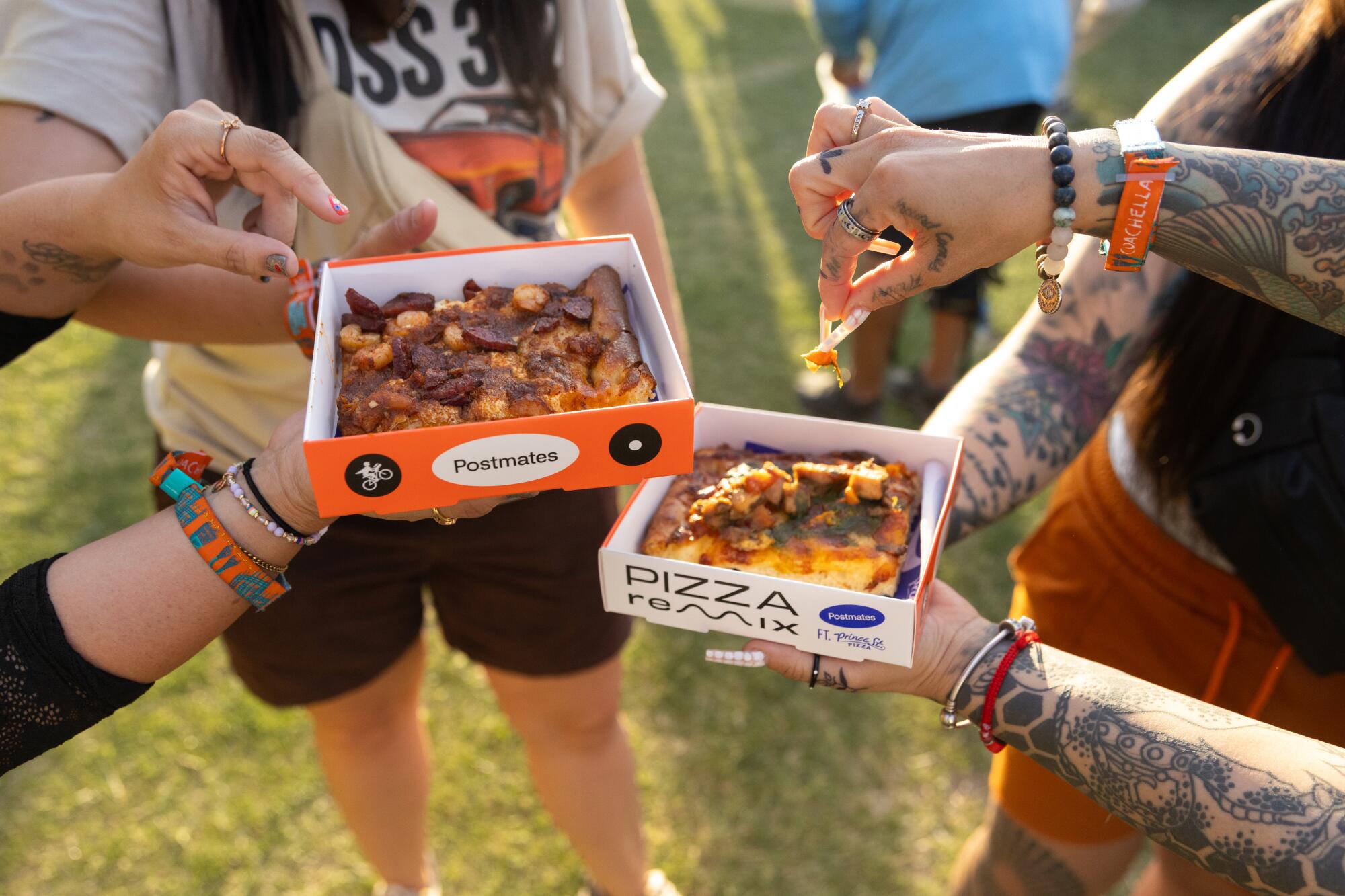 Two people hold boxes with slices of pizza from Postmates Pizza Remix pop-up at Coachella