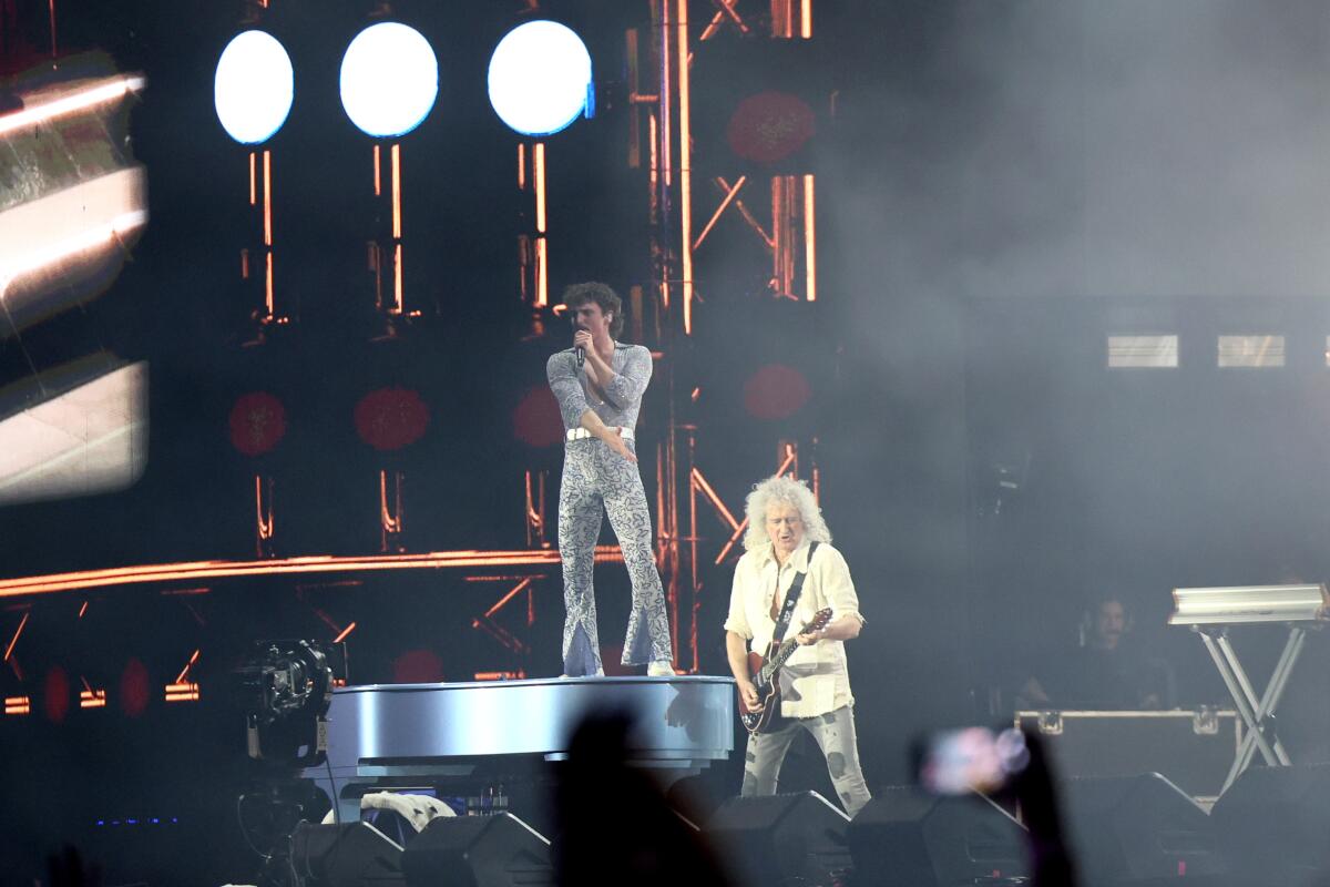 Benson Boone stands on a piano next to Queen guitarist Brian May