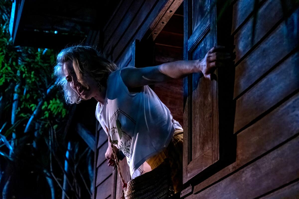 A woman in a T-shirt leaning over the ledge of a window sill.