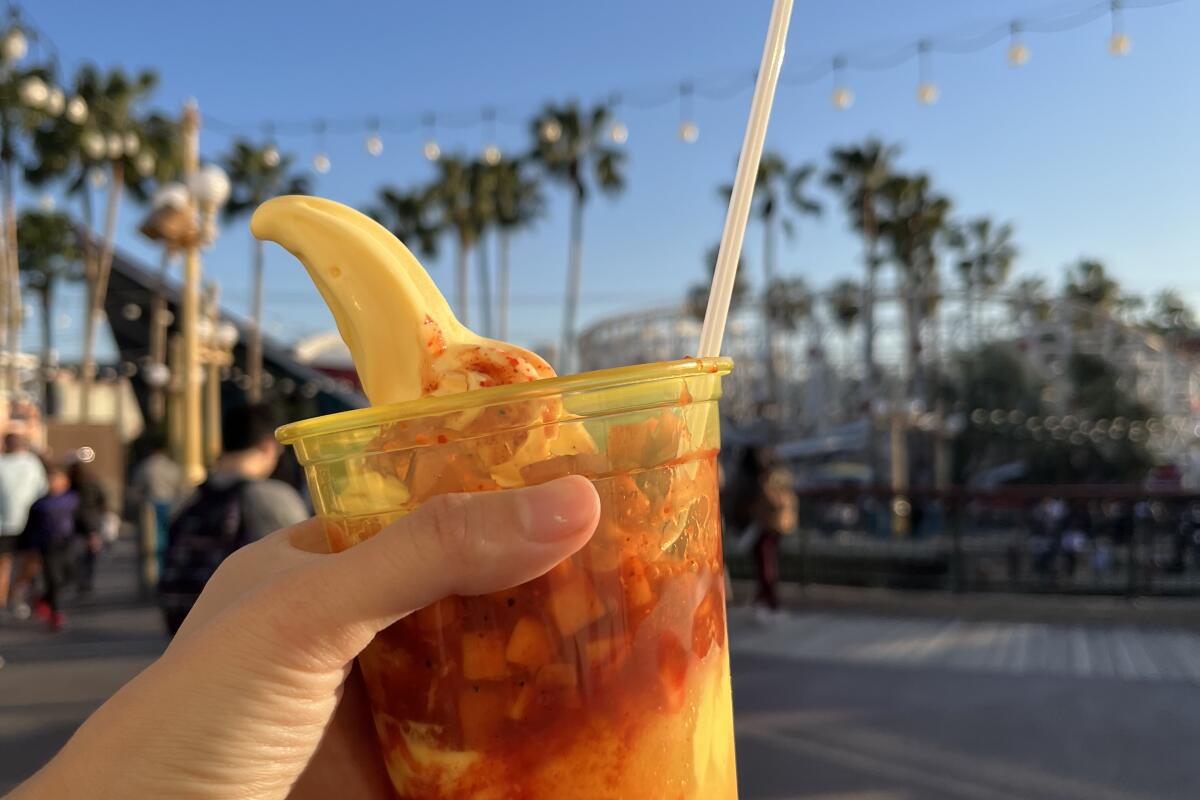 A cup with soft serve held up before a line of palm trees