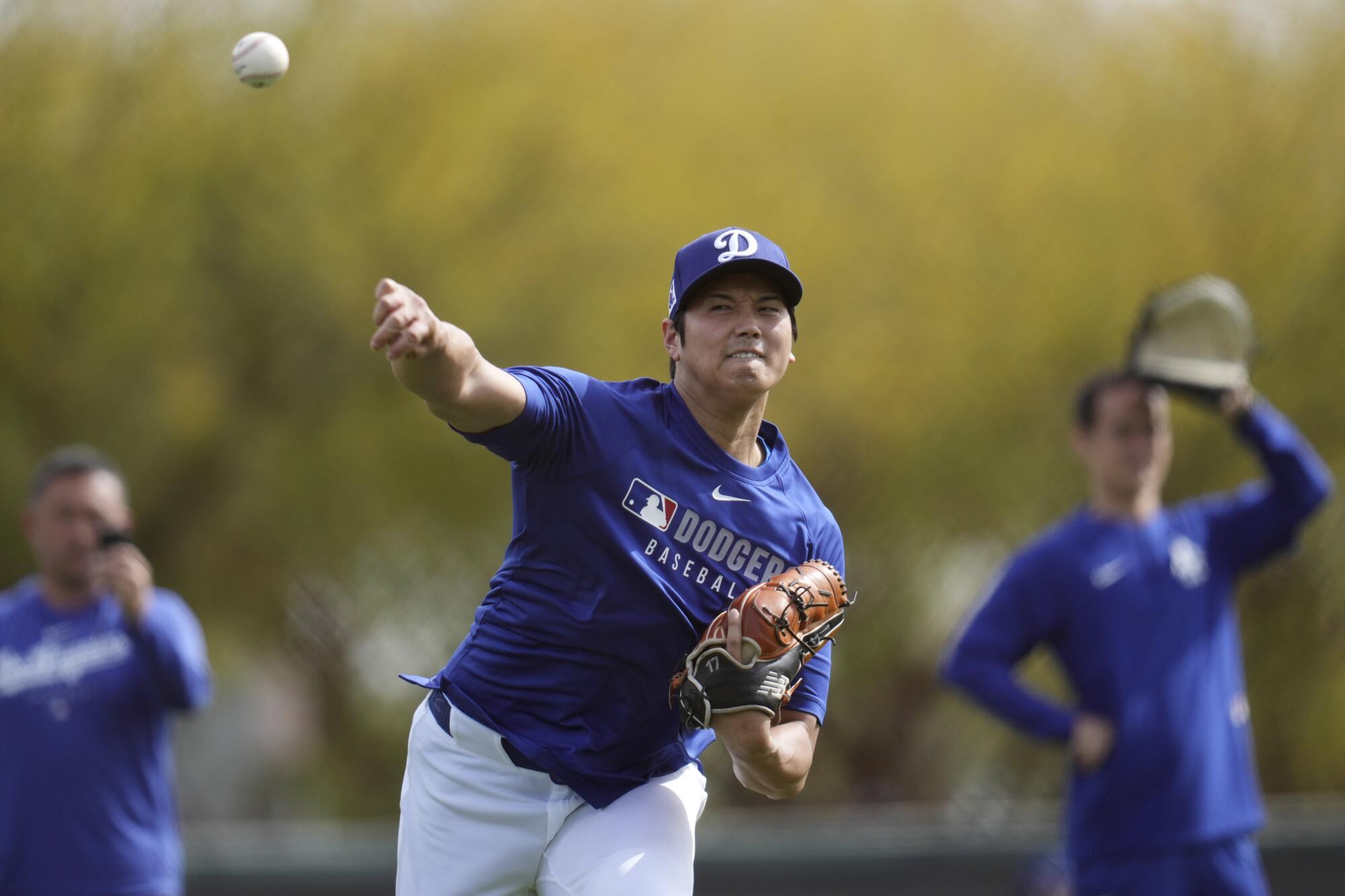 Dodgers star Shohei Ohtani throws the ball as he warms up with other pitchers and catchers