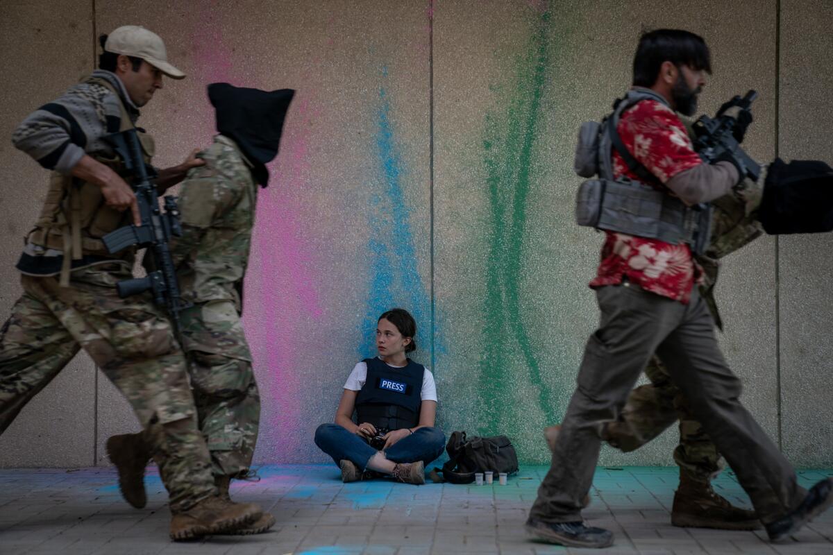 A photojournalist sits on the ground as prisoners of war are led away in hoods.