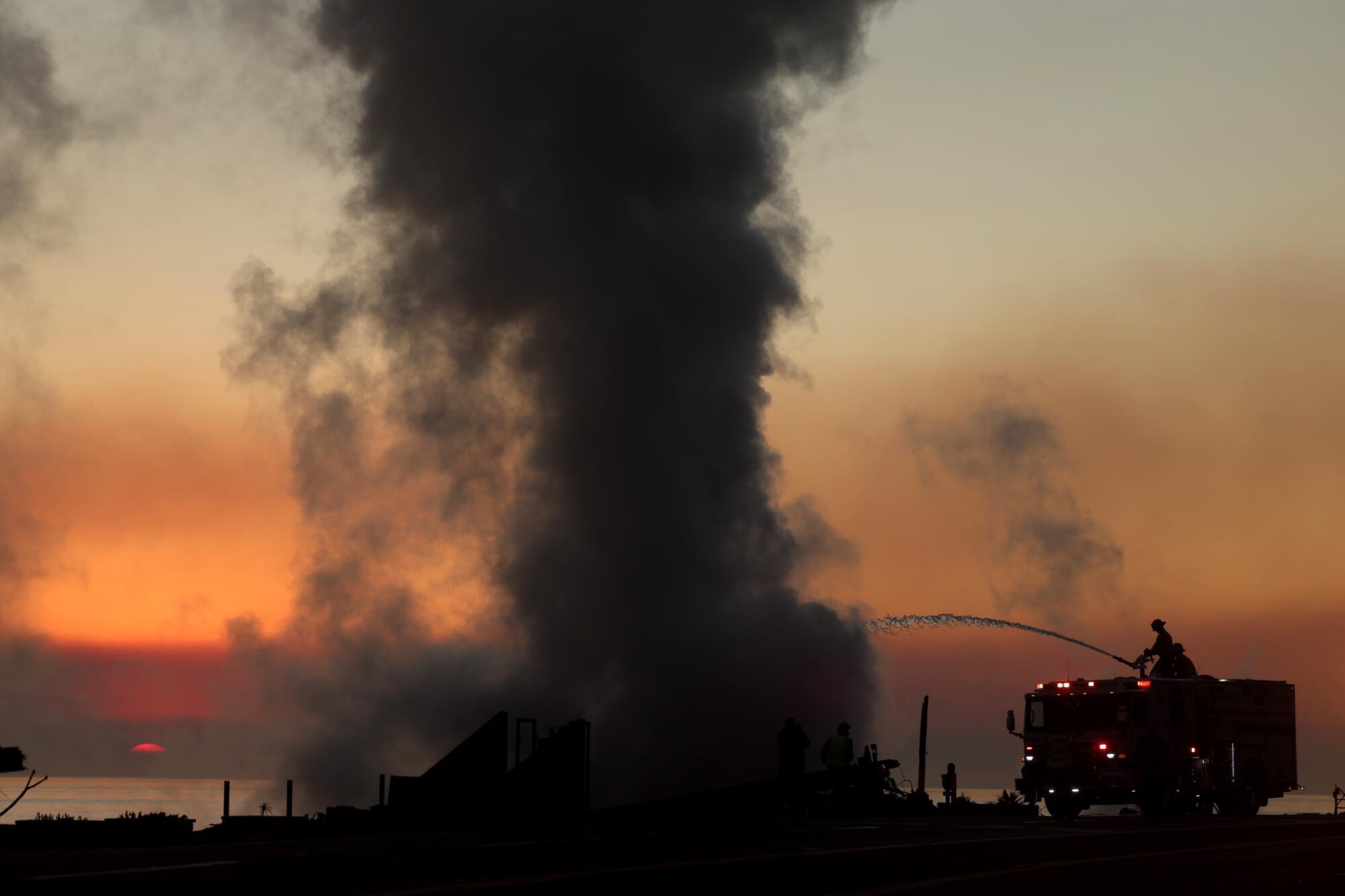 Firefighters put water on a burned-down house in Malibu.