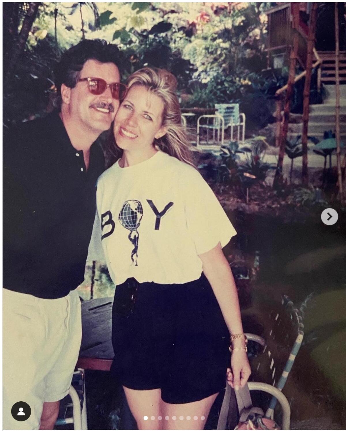 A screenshot of a man and a woman standing outdoors and leaning cheek to cheek