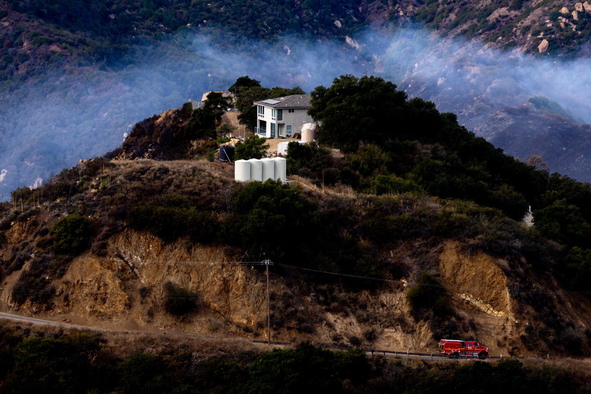 Smoke drifts over a home on Piuma Road as firefighters continue to battle the Franklin fire in Malibu. More photos