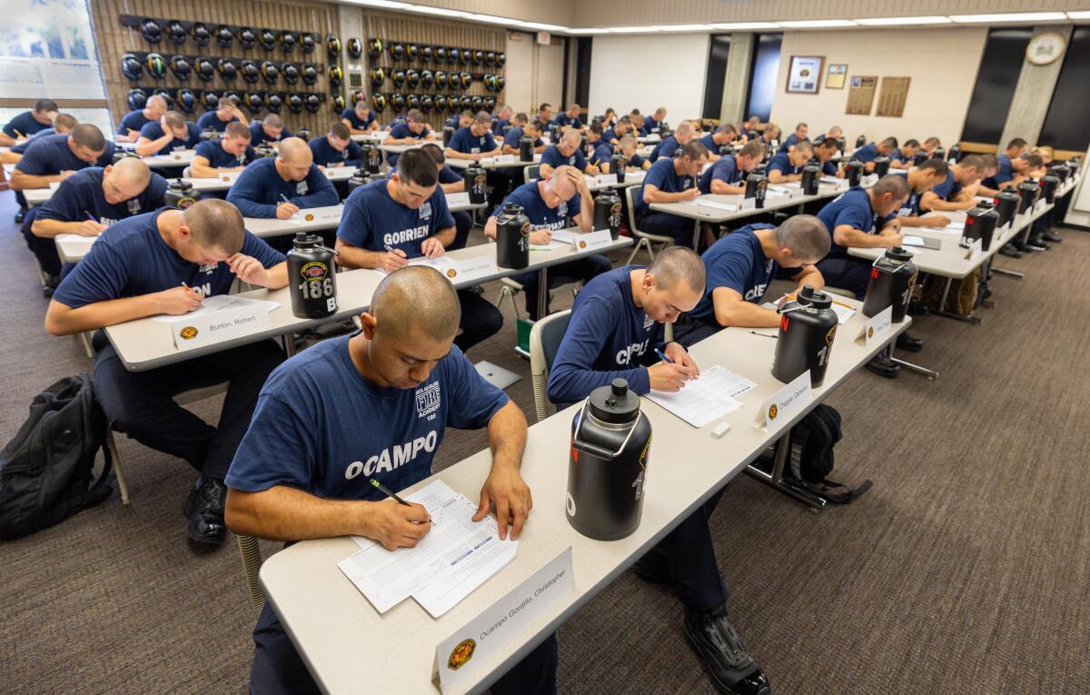 Rows of people sitting at desks write on pieces of paper.